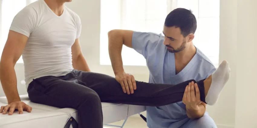 Physiotherapist flexing and stabilizing a patient's leg during a physical therapy session on an exam table.